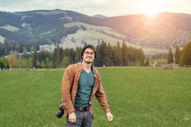 Genç bir adam dağlarda kamerayla gezer.