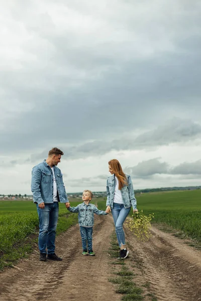 Full growth shot young family in denim casual clothes walking around the park holding hands on warm spring day