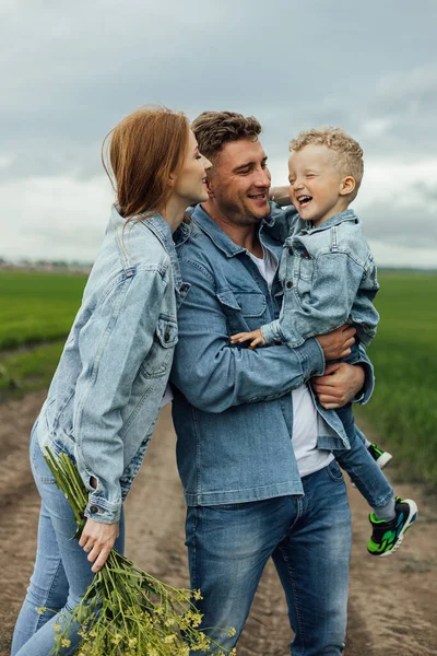 Full growth shot young family in denim casual clothes walking around the park holding hands on warm spring day