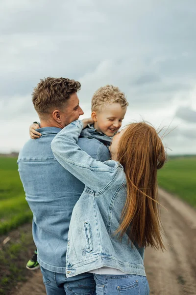 Full growth shot young family in denim casual clothes walking around the park holding hands on warm spring day