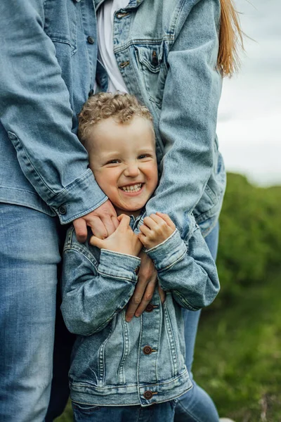 Full growth shot young family in denim casual clothes walking around the park holding hands on warm spring day