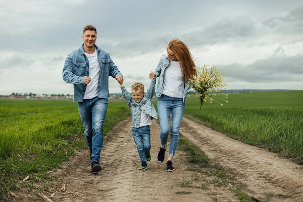 Full growth shot young family in denim casual clothes walking around the park holding hands on warm spring day