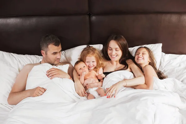 Happy family lying under blanket in bed at home