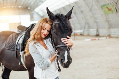 beautiful blond professional female jockey standing near horse. woman horse rider is preparing to equitation. girl and horse. equestrian sport concept. riding vacation.friendship with horse.copy space