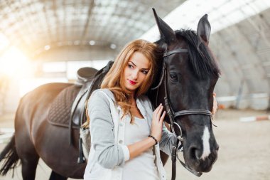 beautiful blond professional female jockey standing near horse. woman horse rider is preparing to equitation. girl and horse. equestrian sport concept. riding vacation.friendship with horse.copy space