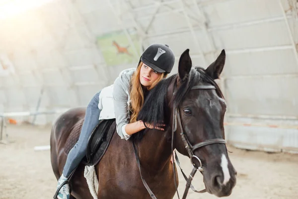 beautiful blond professional female jockey standing near horse. woman horse rider is preparing to equitation. girl and horse. equestrian sport concept. riding vacation.friendship with horse.copy space