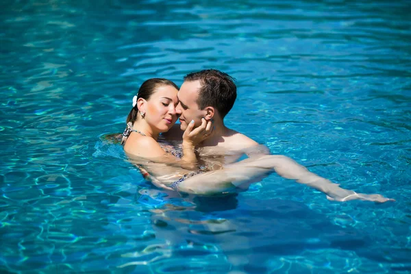 Genç ve seksi çift yüzme havuzunda sarılma. Kız geri eğilir. Arzu gözlerinin içine bakarak adam. Rüya tatil tropikal ülkede. Otelde Yüzme Havuzu