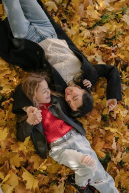 Annesi ile birlikte güpegündüz, sonbahar parkında sarı yapraklarda yatan kız. 