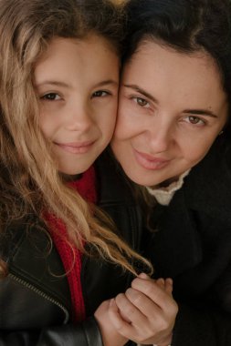 Gündüz vakti, sonbahar parkında annesiyle el ele tutuşan bir kız. 