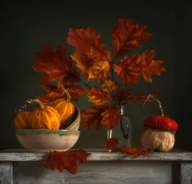 Vazoda sonbahar yaprakları olan bir dal. Yapraklarda sonbahar renkleri. Olgun küçük balkabakları. Eski soyulan sürahi