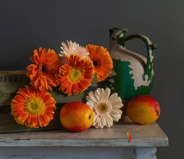 Tahta bir kutuda çiçek açan gerberalar ve olgun elmalar..