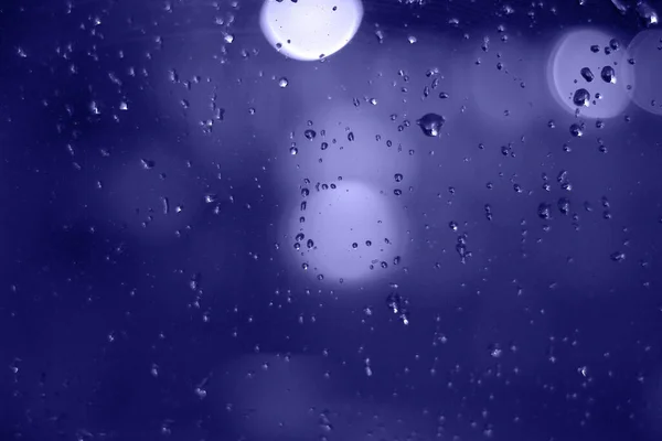 Az esőcseppek bokeh hatással vannak az éjszakai városra. Eső cseppek az ablakban elvont fényekkel. — Stock Fotó