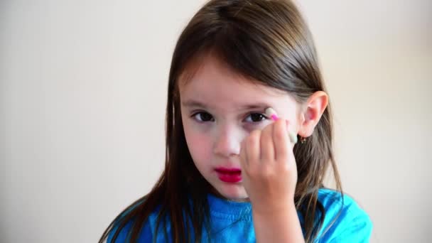 Klein meisje schildert haar ogen met make-up. Klein meisje 4-5 jaar oud zet make-up op haar gezicht — Stockvideo