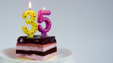 Appetizing birthday cake with burning candles for 35th anniversary on a white rotating plate