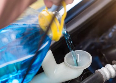 Bir adam arabanın tankına mavi bir cam temizleyici döker. Kapat..