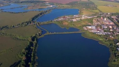 Yazın göllerin üzerinden güzel bir uçuş. Şehir manzarası, yukarıdan binalar. Tarlalar ve ağaçlar yeşillikte gömülüdür..