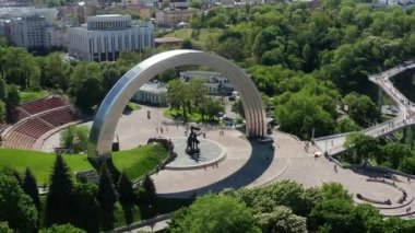 Kiev 'de yaz uçuşu, Halkın Dostluk Kemeri üzerinde, yaya köprüsü, yeşil yapraklarla kaplı ağaç taçları. Ukrayna 'nın başkentinde insanlar ve turistler dolaşıyor.