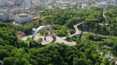 Kiev 'de yaz uçuşu, Halkın Dostluk Kemeri üzerinde, yaya köprüsü, yeşil yapraklarla kaplı ağaç taçları. Ukrayna 'nın başkentinde insanlar ve turistler dolaşıyor.