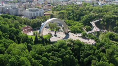 Kiev 'de yaz uçuşu, Halkın Dostluk Kemeri üzerinde, yaya köprüsü, yeşil yapraklarla kaplı ağaç taçları. Ukrayna 'nın başkentinde insanlar ve turistler dolaşıyor.
