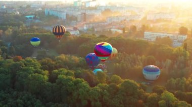 Parkta uçan balonları aydınlatan güzel güneş ışınları, yeşil ağaçlar. Arka planda şehir manzarası var. Güzel sabah balonu uçuşu. Şehrin üst manzarası, orman..