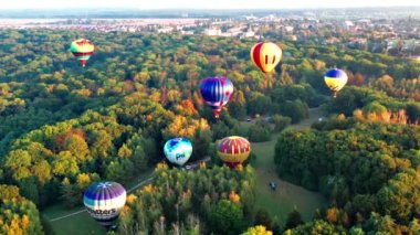 Parkta uçan balonları aydınlatan güzel güneş ışınları, yeşil ağaçlar. Arka planda şehir manzarası var. Güzel sabah balonu uçuşu. Şehrin üst manzarası, orman..