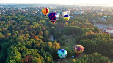 Parkta uçan balonları aydınlatan güzel güneş ışınları, yeşil ağaçlar. Arka planda şehir manzarası var. Güzel sabah balonu uçuşu. Şehrin üst manzarası, orman..