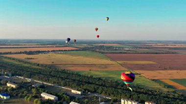 Çok renkli balonlar tarlaların, evlerin, ağaçların üzerinde uçuyor. Mavi gökyüzü.