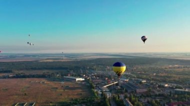 Çok renkli balonlar tarlaların, evlerin, ağaçların üzerinde uçuyor. Mavi gökyüzü.