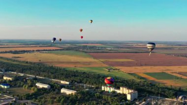 Çok renkli balonlar tarlaların, evlerin, ağaçların üzerinde uçuyor. Mavi gökyüzü.