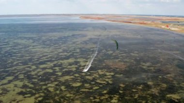 İnsanlar denizde uçurtma gibi uçuyor. Rüzgar sporcuyu deniz dalgaları boyunca taşır. Çok renkli paraşütler. Yukarıdan, bir kuadrokopterden uçurtmacılara görüntüle.