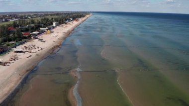 Yazın sahilde güzel bir uçuş. İnsanlar deniz kenarında dinleniyor. Turistler için evler. Plaj şemsiyeleri, gezintiler, denizde yüzen insanlar..