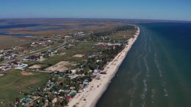 Yazın sahilde güzel bir uçuş. İnsanlar deniz kenarında dinleniyor. Turistler için evler. Plaj şemsiyeleri, gezintiler, denizde yüzen insanlar..