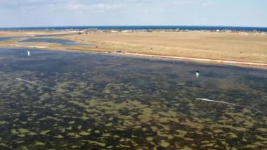 İnsanlar denizde uçurtma gibi uçuyor. Rüzgar sporcuyu deniz dalgaları boyunca taşır. Çok renkli paraşütler. Yukarıdan, bir kuadrokopterden uçurtmacılara görüntüle.