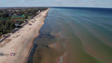 Yazın sahilde güzel bir uçuş. İnsanlar deniz kenarında dinleniyor. Turistler için evler. Plaj şemsiyeleri, gezintiler, denizde yüzen insanlar..