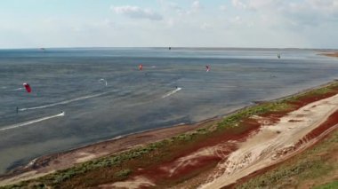 İnsanlar denizde uçurtma gibi uçuyor. Rüzgar sporcuyu deniz dalgaları boyunca taşır. Çok renkli paraşütler. Yukarıdan, bir kuadrokopterden uçurtmacılara görüntüle.