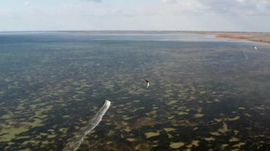 İnsanlar denizde uçurtma gibi uçuyor. Rüzgar sporcuyu deniz dalgaları boyunca taşır. Çok renkli paraşütler. Yukarıdan, bir kuadrokopterden uçurtmacılara görüntüle.