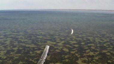 İnsanlar denizde uçurtma gibi uçuyor. Rüzgar sporcuyu deniz dalgaları boyunca taşır. Çok renkli paraşütler. Yukarıdan, bir kuadrokopterden uçurtmacılara görüntüle.