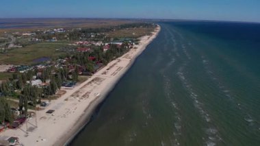 Yazın sahilde güzel bir uçuş. İnsanlar deniz kenarında dinleniyor. Turistler için evler. Plaj şemsiyeleri, gezintiler, denizde yüzen insanlar..