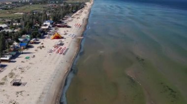 Yazın sahilde güzel bir uçuş. İnsanlar deniz kenarında dinleniyor. Turistler için evler. Plaj şemsiyeleri, gezintiler, denizde yüzen insanlar..