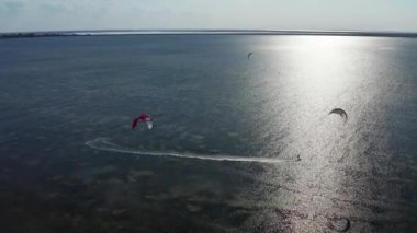 İnsanlar denizde uçurtma gibi uçuyor. Rüzgar sporcuyu deniz dalgaları boyunca taşır. Çok renkli paraşütler. Yukarıdan, bir kuadrokopterden uçurtmacılara görüntüle.