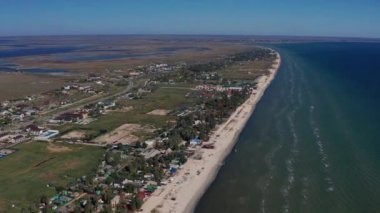Yazın sahilde güzel bir uçuş. İnsanlar deniz kenarında dinleniyor. Turistler için evler. Plaj şemsiyeleri, gezintiler, denizde yüzen insanlar..