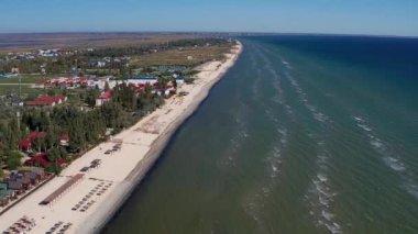 Yazın sahilde güzel bir uçuş. İnsanlar deniz kenarında dinleniyor. Turistler için evler. Plaj şemsiyeleri, gezintiler, denizde yüzen insanlar..