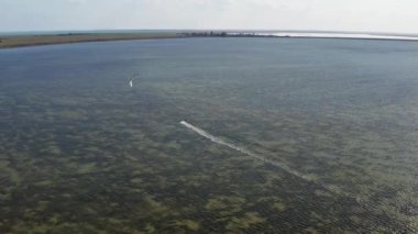 İnsanlar denizde uçurtma gibi uçuyor. Rüzgar sporcuyu deniz dalgaları boyunca taşır. Çok renkli paraşütler.