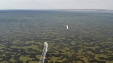 İnsanlar denizde uçurtma gibi uçuyor. Rüzgar sporcuyu deniz dalgaları boyunca taşır. Çok renkli paraşütler.