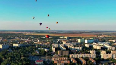 Multicolored balloons fly over trees. Nice top view of the park, forest covered with greenery. Beautiful blue sky and top view of the city, houses.