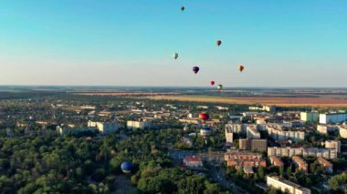 Multicolored balloons fly over trees. Nice top view of the park, forest covered with greenery. Beautiful blue sky and top view of the city, houses.