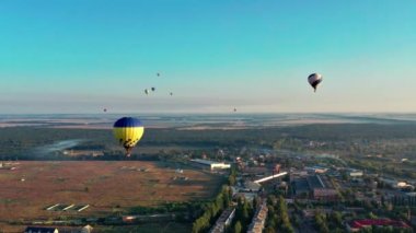 Multicolored balloons fly over trees. Nice top view of the park, forest covered with greenery. Beautiful blue sky and top view of the city, houses.