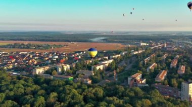 Multicolored balloons fly over trees. Nice top view of the park, forest covered with greenery. Beautiful blue sky and top view of the city, houses.