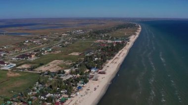 Yazın sahilde güzel bir uçuş. İnsanlar deniz kenarında dinleniyor. Turistler için evler. Plaj şemsiyeleri, gezintiler, denizde yüzen insanlar..