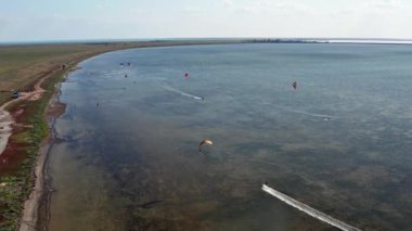 İnsanlar denizde uçurtma gibi uçuyor. Rüzgar sporcuyu deniz dalgaları boyunca taşır. Çok renkli paraşütler.